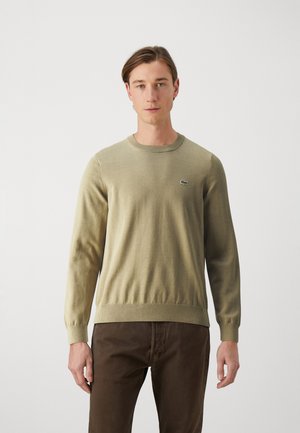 Maglione lavorato a maglia verde oliva con maniche lunghe, polsini a coste e orlo a coste. Presenta un piccolo logo verde sul petto.