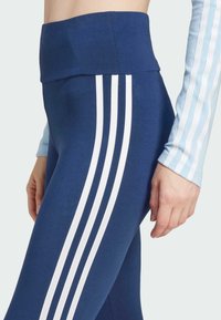 Marinblå högmidjade leggings med tre vita vertikala ränder längs sidorna. Slät, elastisk tyg med en figursydd silhuett.