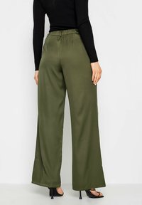 Olijfgroene broek met wijde pijpen, gemaakt van gladde stof. Heeft een elastische tailleband en een enkel-lengte snit. Geen zichtbare patronen of accenten.