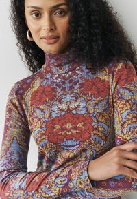 Pulover cu guler înalt, multicolor, cu modele florale în roșu, albastru și galben. Formă ajustată, cu mâneci lungi și un material texturat.