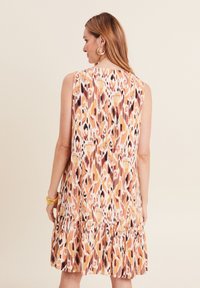 Ärmelloses Kleid mit einem Rüschen-Saum in einem bunten, abstrakten Muster aus Orange, Pink und Braun auf einem hellen Hintergrund. Weicher, strukturierter Stoff.