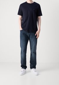 Camiseta de algodón azul marino de manga corta, combinada con jeans de mezclilla azules y zapatillas blancas. Diseño simple sin patrones ni logotipos visibles.
