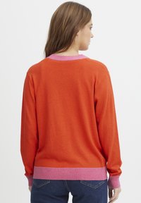 Stickad tröja i orange med en rosa ribbad krage och mudd, har lång ärm och en avslappnad passform. Texturerad stickad mönster är tydlig.