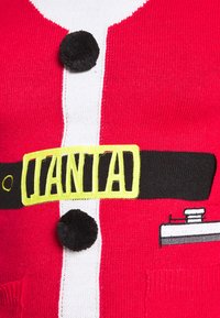 Červený pletený svetr s bílým pruhem, černými knoflíky a žlutým páskem s textem "SANTA". Textura je hladká a design je hravý.