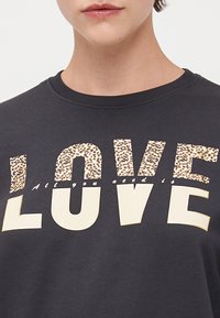 Dark gray sweatshirt featuring the word "LOVE" in bold with leopard print accent and smaller text below stating "All you need is."