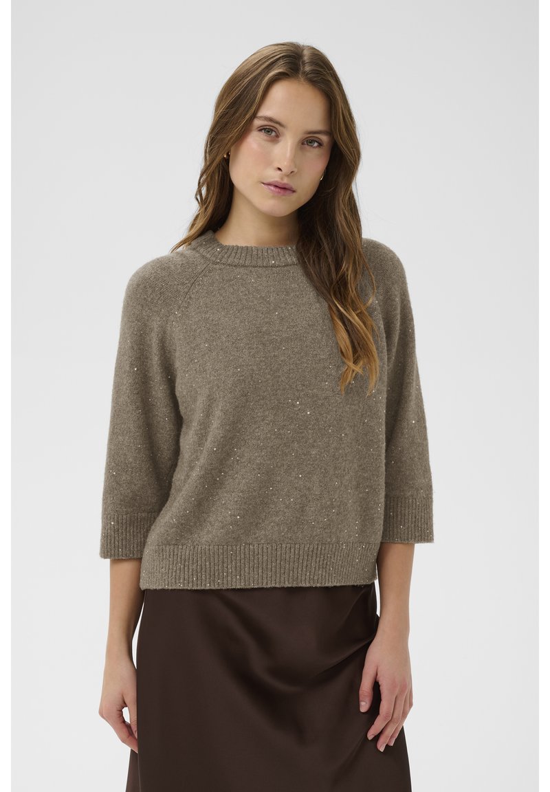 Barna kötött pulóver kerek nyakkivágással, háromnegyedes ujjakkal és finom pettyekkel, elegáns barna szatén szoknyával párosítva.