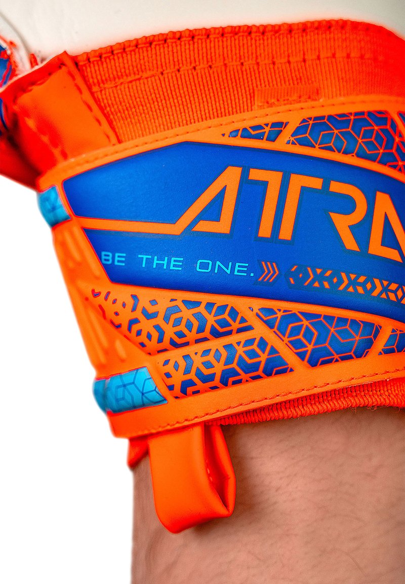 Correa deportiva naranja y azul con un patrón texturizado, presenta un logo "ATR" y la frase "BE THE ONE." El material parece sintético.