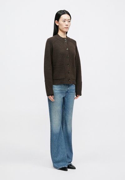 Pruun kootud kardigan pikkade varrukatega, ees nööbitav, kahe küljetaskuga, kombineeritud laia säärega heleroheliste teksade ja teravate mustade jalanõudega.