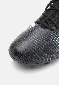 Botas de fútbol negras con una superficie texturizada, que presentan un patrón degradado, puntera redonda y cordones negros. Diseñadas para proporcionar agarre en el césped.