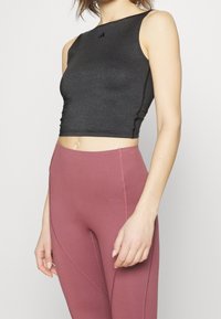 Crop top noir ajusté avec un col montant et un accent logo, associé à un legging rose taille haute avec des détails de coutures et un logo.