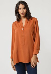 Camisa de manga larga color óxido con cuello con muesca y tapeta de botones en la parte frontal. Tejido suave y liso con un corte relajado y aberturas laterales.