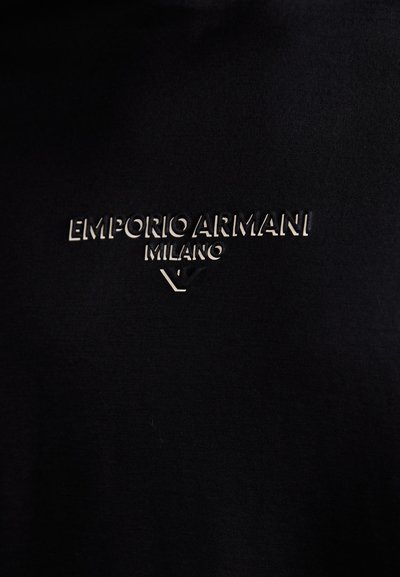 T-shirt noir en tissu doux, avec un logo embossé "EMPORIO ARMANI MILANO" en argent. Design simple à col rond.