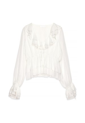 Blusa bianca a maniche lunghe con volant sovrapposti sul colletto, sui polsini e sull'orlo, dotata di scollatura a V e laccetto da annodare sul davanti.