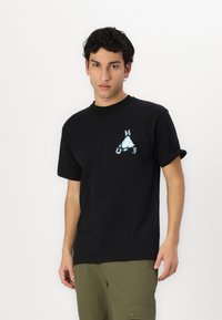 Black cotton t-shirt featuring a partially visible blue graphic print with the letters "H," "U," and "F" in a triangle shape. Short sleeves.