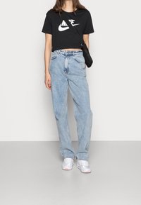 Černé zkrácené tričko Nike, světle modré volné džíny s vybledlým vzhledem a bílé tenisky s růžovými akcenty. Připevněná černá kabelka na rameno.