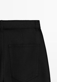 Bagfra visning af sort denimnederdel, der viser linning, bæltestropper og en enkelt firkantet baglomme på hvid baggrund.