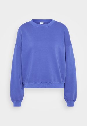 Sudadera azul con cuello redondo, hombros caídos y puños acanalados. Textura suave con un diseño liso, etiqueta de logo en el cuello.