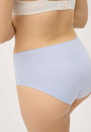 Parte baja de la espalda y caderas de una mujer con ropa interior sin costuras de color azul claro y un sujetador blanco, vista desde atrás contra un fondo liso.