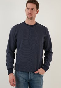 Tumši zils garām piedurknēm izgatavots džemperis ar tekstūru, ar apaļu kakla izgriezumu un ribotiem piedurkņu galiem. Kombinēts ar gaiši ziliem džinsiem.