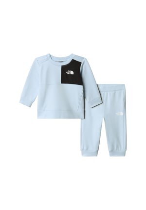 Lys blå genser og matchende bukser laget av mykt stoff. Har en svart brystpanel med logo. Elastiske mansjetter og midjebånd.