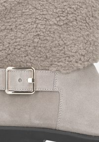 Bottine en suède gris avec un col en tissu texturé moelleux et un accent de boucle rectangulaire en métal sur le côté, avec une semelle en caoutchouc noire.