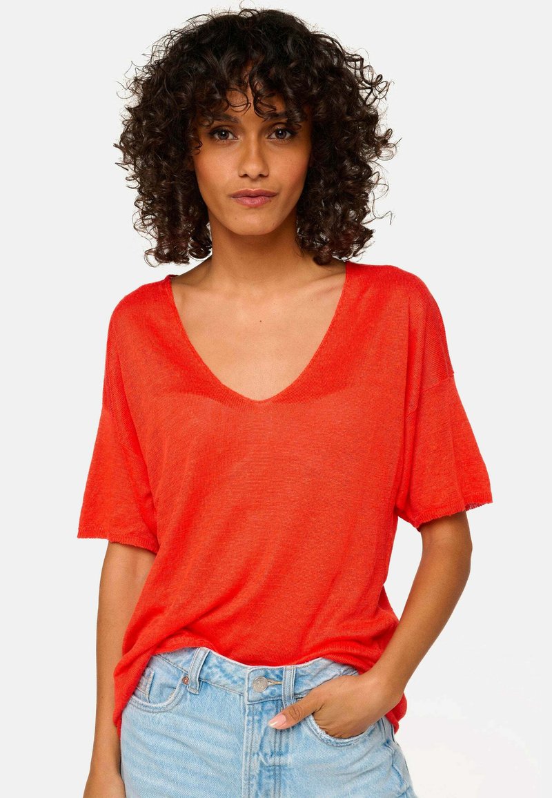 Red, short-sleeve V-neck t-shirt made of lightweight fabric; features a relaxed fit and frayed hem. Paired with light-wash denim.