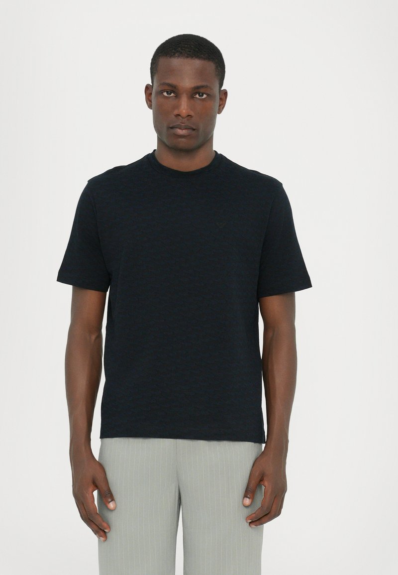 T-shirt noir à manches courtes avec un motif texturé subtil, col rond et coupe décontractée, associé à un pantalon rayé gris clair.