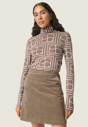 Braun gemusterter Rollkragenpullover mit weißen geometrischen Designs, kombiniert mit einem braunen Cord-Minirock, der eine weiche Textur aufweist.