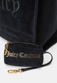 Crna kordura torba s zlatnim logotipom "Juicy Couture", s malom torbicom na patentni zatvarač i kopčom za praktičnost.