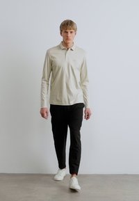 Μακρυμάνικο, ανοιχτό μπεζ πόλο με γιακά, συνδυασμένο με μαύρο παντελόνι και λευκά αθλητικά παπούτσια. Απλό, ελαστικό ύφασμα. Απλός σχεδιασμός.