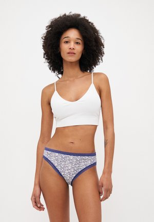 Top scurt alb cu dungi, cu bretele subțiri, asortat cu chiloți de bikini cu model, având un tiv albastru și desen abstract în nuanțe de bleumarin și alb.