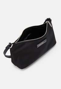 Pochette en nylon noir avec une fermeture éclair argentée. Dispose d'une plaque avec le logo Calvin Klein et d'une bandoulière amovible pour un porté polyvalent.