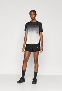 Αθλητικό τοπ σε ασπρόμαυρο με διαβαθμισμένο σχέδιο, με λεπτομέρεια από δίχτυ στον ώμο, συνδυασμένο με μαύρο σορτς και μαύρα αθλητικά παπούτσια.