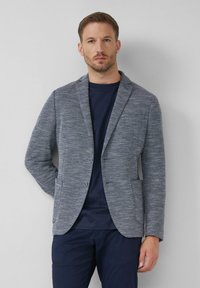 Grauer gewebter Blazer mit Revers, zwei Knöpfen und seitlichen Taschen, über einem marineblauen T-Shirt mit strukturiertem Finish getragen.