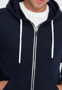 Námořnická mikina s kapucí na zip vyrobená z bavlněné směsi, se bílými stahovacími šňůrkami, předním zipem a klokaní kapsou.