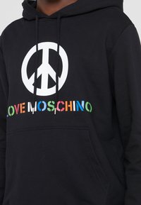 Black hooded sweatshirt featuring a large white peace sign and colorful "LOVE MOSCHINO" text across the front. Soft fabric, relaxed fit.