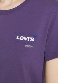 Fialové bavlněné tričko s bílým logem Levi's v modrém obrysu. Kulatý výstřih a krátké rukávy s hladkým povrchem.