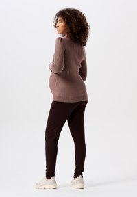 Zwangere trui in lichtbruin rib gebreid met pofmouwen, gecombineerd met donkergroene aansluitende broek en witte sneakers.