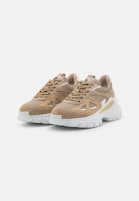 Sneaker in suede beige e mesh con suola in gomma bianca. Presenta elementi di design ritagliati e un accento giallo sul lato. Chiusura con lacci.