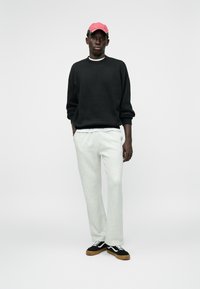 Sudadera negra, pantalones de chándal grises y zapatillas negras con suelas de goma. Gorra roja con un patrón. Look casual con cinturilla elástica.