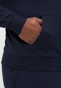 Σκούρο μπλε φούτερ με μπροστινή τσέπη, ριγέ μανσέτες και υφασμάτινη επιφάνεια, με λεία φινίρισμα και δομημένη βάση.