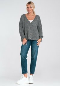 Szary sweter zapinany na guziki z dekoltem w serek i teksturowanym materiałem. Połączony z niebieskimi dżinsami i białymi trampkami.