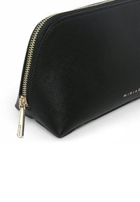 Czarna kosmetyczka o teksturowanej powierzchni z złotym zamkiem, o kształcie trójkąta i metalowym logo z boku. Gładki, trwały materiał.