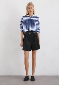 Blauw-wit gestreepte lange mouw shirt, zwarte hoge taille shorts en zwarte instappers. Glad materiaal, ontspannen pasvorm en klassiek ontwerp.
