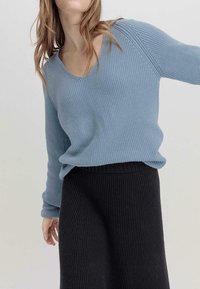 Suéter de punto azul claro con escote en V y textura acanalada, combinado con una falda negra acanalada. El suéter tiene mangas largas y un corte holgado.