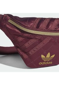 Maroon waist bag with a quilted texture, gold zipper, and Adidas logo. Features a wide adjustable strap for secure wear.