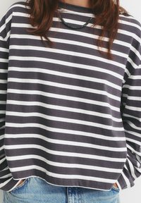 Grau-weiß gestreifter Langarmpullover mit lockerer Passform, runder Halslinie und sichtbaren Nähten entlang des Saums.