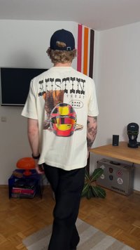 Crèmekleurig T-shirt met een grote afbeelding van een helm en de tekst "AUSTIN TEXAS 2023" op de achterkant, gecombineerd met een zwarte broek.