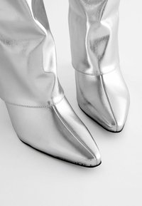 Bottines métalliques argentées avec un design à bout pointu, présentant une texture lisse et brillante ainsi que des coutures subtiles en haut.