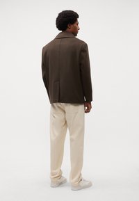 Bruine wollen blend jacket met een opstaande kraag, rechte snit en terugventilatie. Gecombineerd met crèmekleurige broeken en witte sneakers.